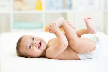 baby lying on white bed and holding legs - obrazy, fototapety, plakaty
