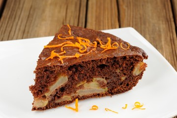 Chocolate apple cake with orange peels on white plate