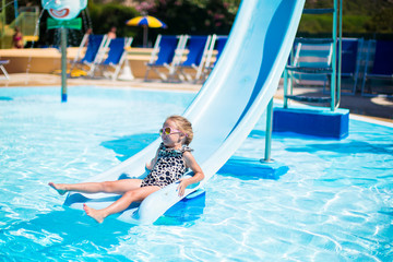 Naklejka premium Little girl on water slide at aquapark on summer holiday
