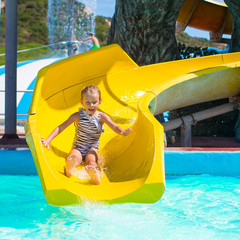 Little girl on water slide at aquapark during summer holiday