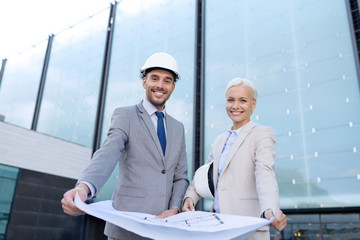 smiling businessmen with blueprint and helmets