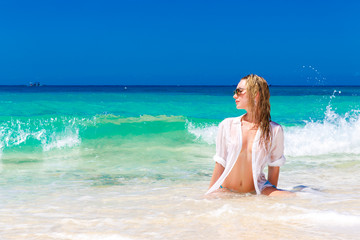 Fototapeta na wymiar Young beautiful girl in wet white shirt on the beach. Blue trop