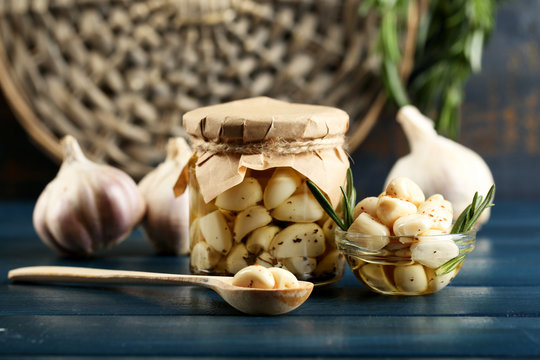 Canned garlic in glass jar on color wooden background