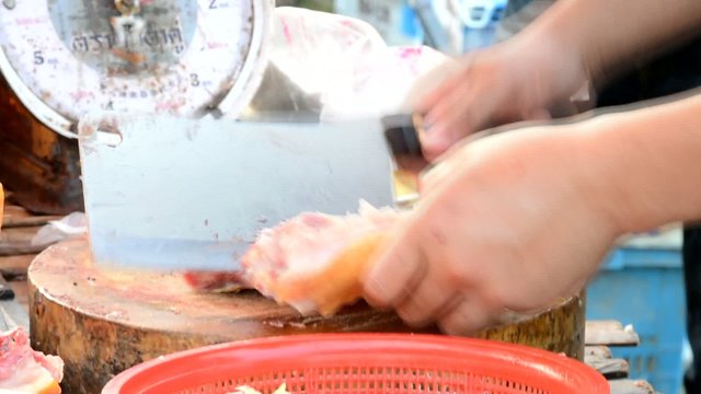 Thai butcher is chopping raw chicken with chopping knife