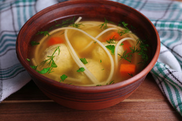 Soup with meatballs and noodles in bowl on wooden background