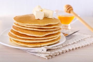 Stack of delicious pancakes with butter and honey in saucer