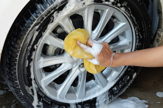 female hand is cleaning car tire with sponge