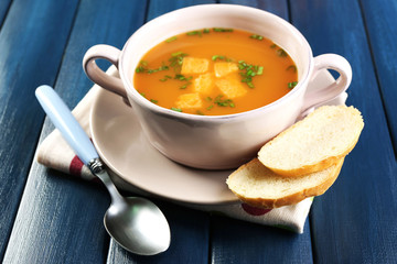 Carrot soup in bowl, on color wooden background