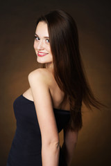 Fototapeta premium Beautiful young woman with long hair on dark brown background