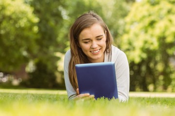 Smiling university student lying and using tablet pc