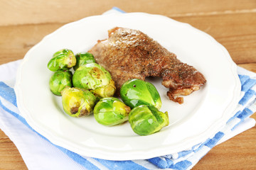 Roasted meat and vegetables on plate, on wooden table