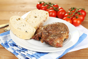 Roasted meat and vegetables on plate, on wooden table