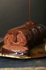 Delicious roll cake on wooden table, on dark background