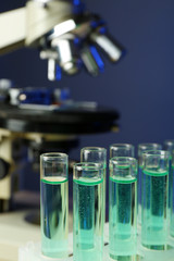 Microscope and test tubes on table, on color background