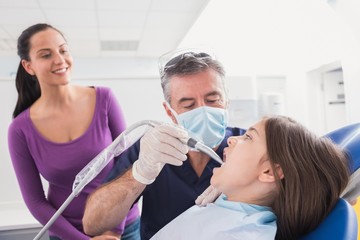 Pediatric dentist examining young patient with a suction tube