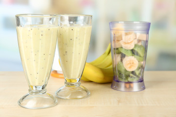 Glasses with milkshake and sliced fruits in bowl of blender