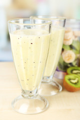 Glasses with milkshake and sliced fruits in bowl of blender