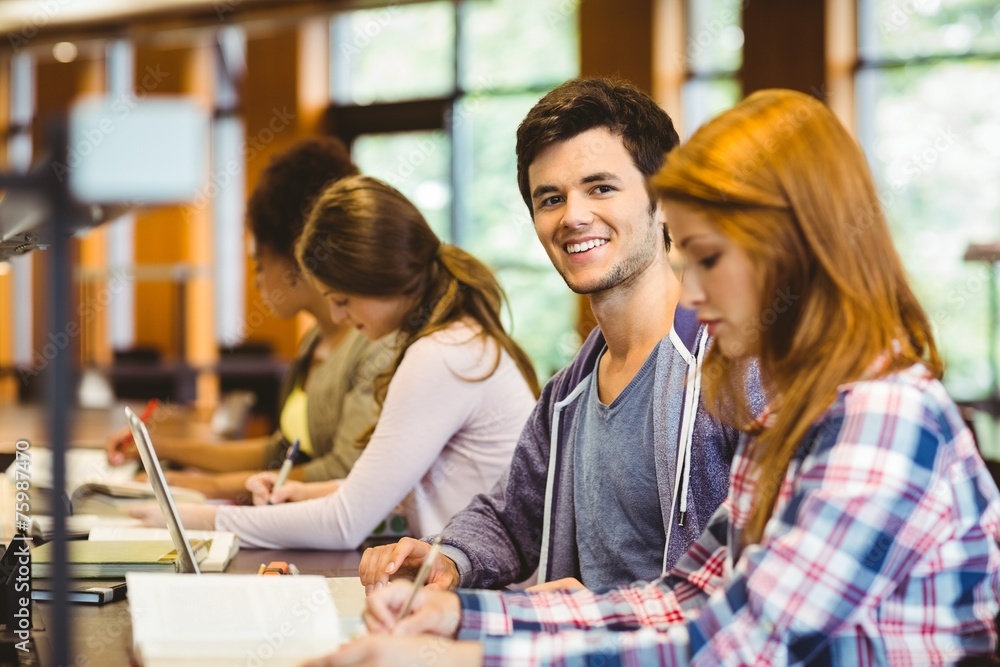 Poster Student looking at camera while studying with classmates