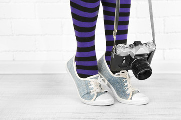 Girl in sneakers with retro photo camera in room