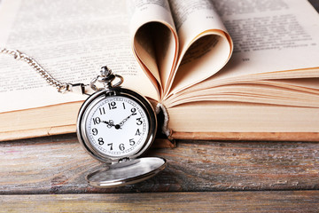 Silver pocket clock and book on wooden table
