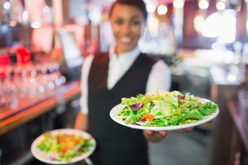 Pretty barmaid holding plates of salads