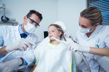 Dentist with assistant examining girls teeth