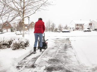 Woman using a snowblower to clear a driveway during snowstorm