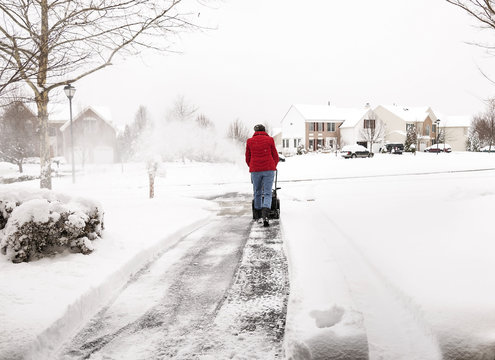 Woman using a snowblower to clear a driveway during snowstorm