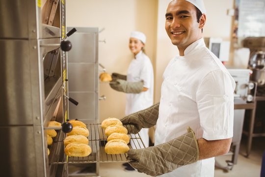 Baker smiling at camera taking rolls out of oven