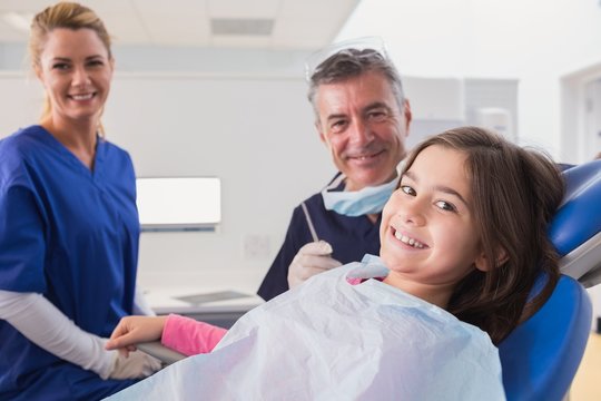 Smiling pediatric dentist and nurse with a young patient