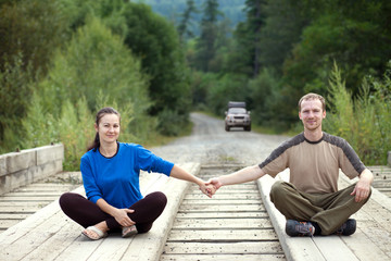Tourist couple sitting on a wooden bridge and holding hands