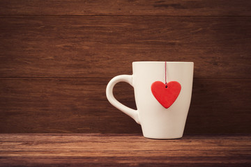 White cup with red heart shape over vintage wooden background