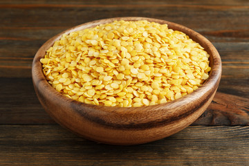 Yellow lentil in a wooden bowl on wood closeup