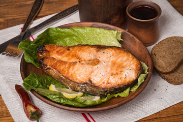 Baked trout steak in pottery with salad and slices of lemon