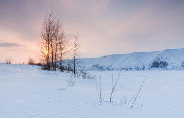 Winter landscape with frozen river and the hilly coast at sunset