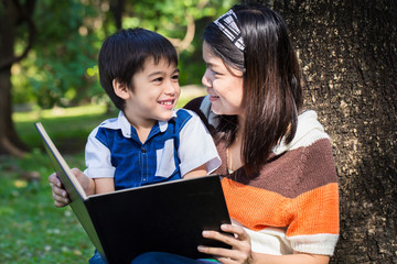 Mother reading a book with her son with smile face in park under