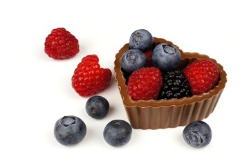 Heart shaped chocolate cup filled with fresh berries over white