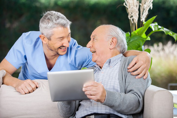 Laughing Caretaker And Senior Man Using Tablet Computer