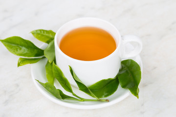 Brewed tea on table top, with freshly harvested tea as props.