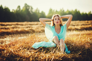 Beautiful blonde girl posing in a field at sunset