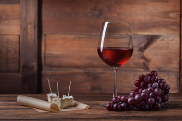 Red wine in glass with grape and cheese on wood