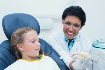 Female dentist teaching girl how to brush teeth