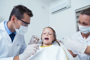 Dentist with assistant examining girls teeth