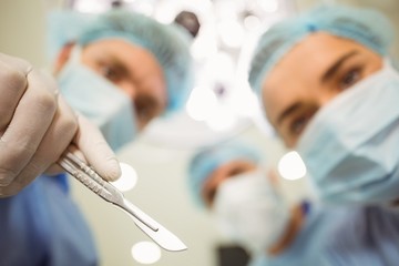 Young surgeons looking down at camera holding scalpel