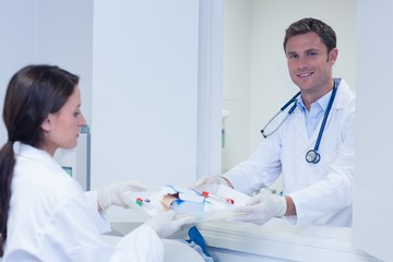 Doctor giving tray with blood sample to his colleague