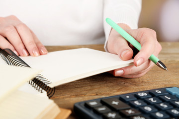 Female hand with pen, notebook and calculator at desktop