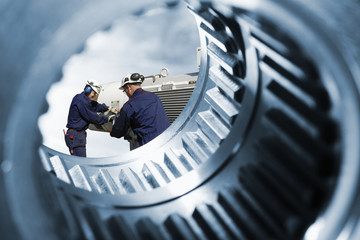 engineers with machinery seen through a giant cogwheels axles
