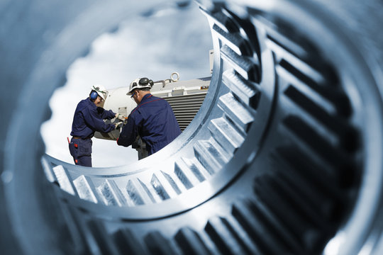 engineers with machinery seen through a giant cogwheels axles
