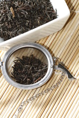 black tea leaves in white bowl with strainer on bamboo mat