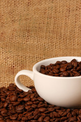 Coffee beans in white cup on brown sack background